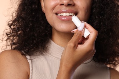 Photo of Smiling woman applying lip balm onto her lips on beige background, closeup