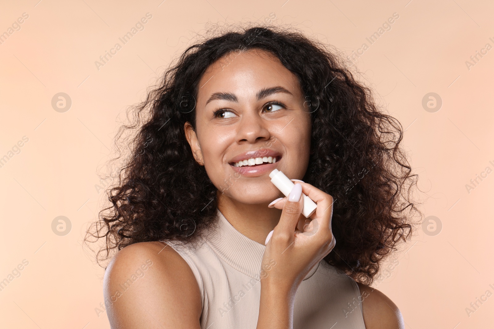 Smiling woman applying lip balm onto her lips on beige background Photo of Smiling woman applying lip balm onto her lips on beige background