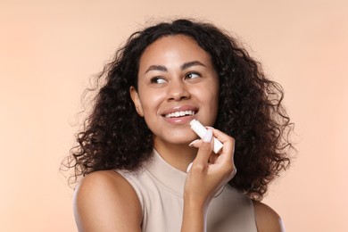 Photo of Smiling woman applying lip balm onto her lips on beige background
