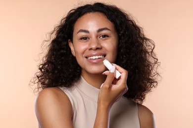 Photo of Smiling woman applying lip balm onto her lips on beige background