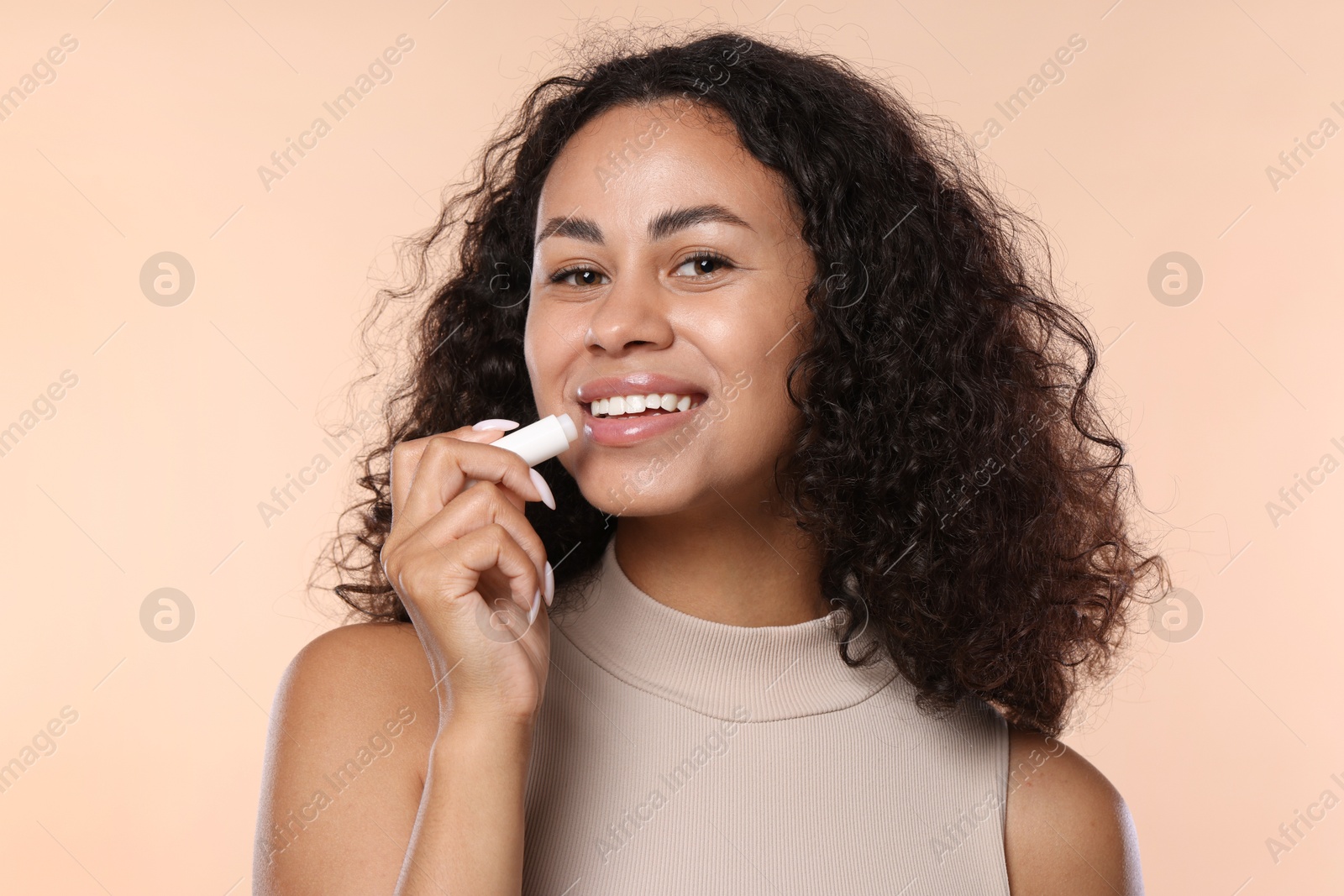 Smiling woman applying lip balm onto her lips on beige background Photo of Smiling woman applying lip balm onto her lips on beige background