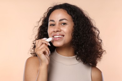 Photo of Smiling woman applying lip balm onto her lips on beige background