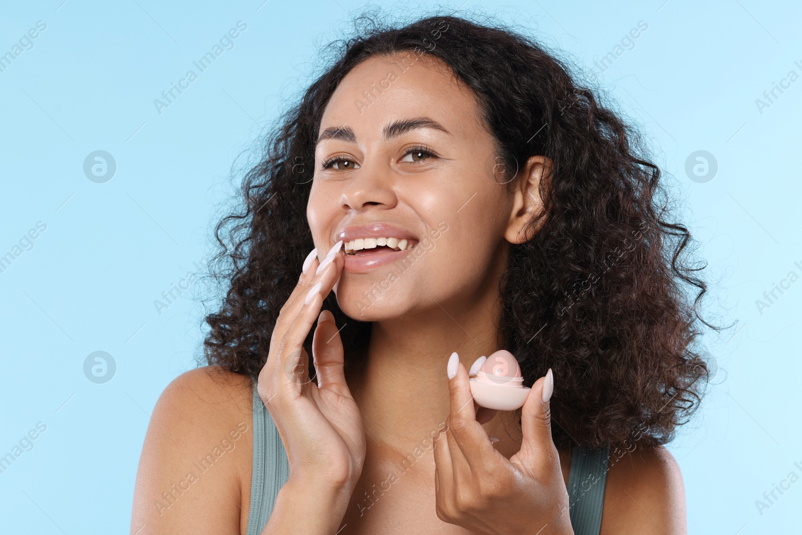Smiling woman with lip balm on light blue background Photo of Smiling woman with lip balm on light blue background