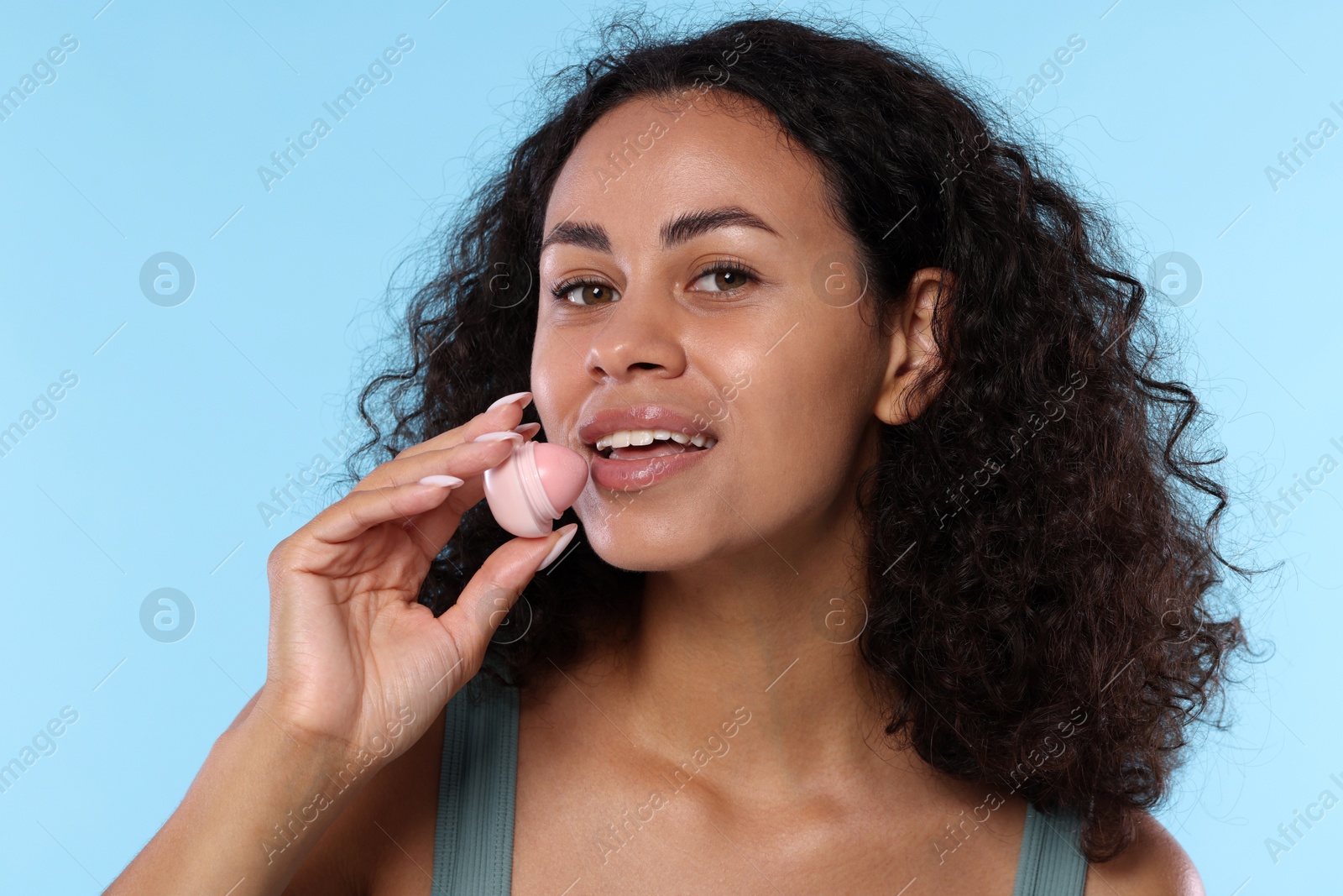 Smiling woman with lip balm on light blue background Photo of Smiling woman with lip balm on light blue background
