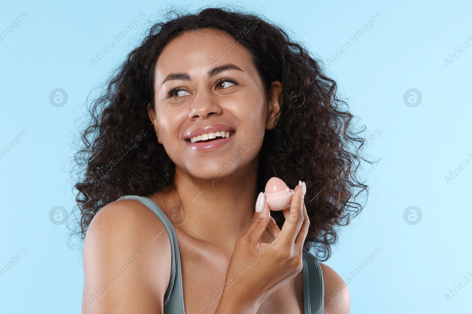 Smiling woman with lip balm on light blue background Photo of Smiling woman with lip balm on light blue background
