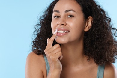 Photo of Smiling woman applying lip balm onto her lips on light blue background, closeup