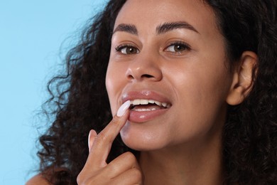 Photo of Smiling woman applying lip balm onto her lips on light blue background, closeup