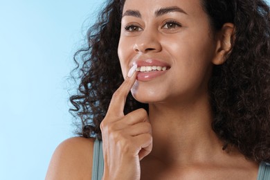 Photo of Smiling woman applying lip balm onto her lips on light blue background, closeup