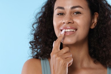 Photo of Smiling woman applying lip balm onto her lips on light blue background, closeup