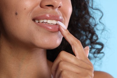 Photo of Smiling woman applying lip balm onto her lips on light blue background, closeup
