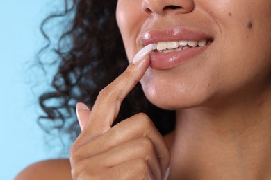 Photo of Smiling woman applying lip balm onto her lips on light blue background, closeup