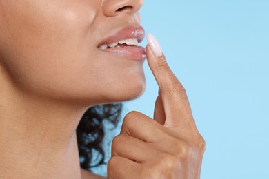 Photo of Smiling woman applying lip balm onto her lips on light blue background, closeup. Space for text