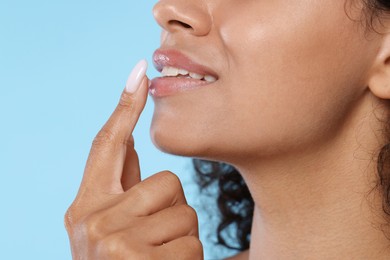 Photo of Smiling woman applying lip balm onto her lips on light blue background, closeup