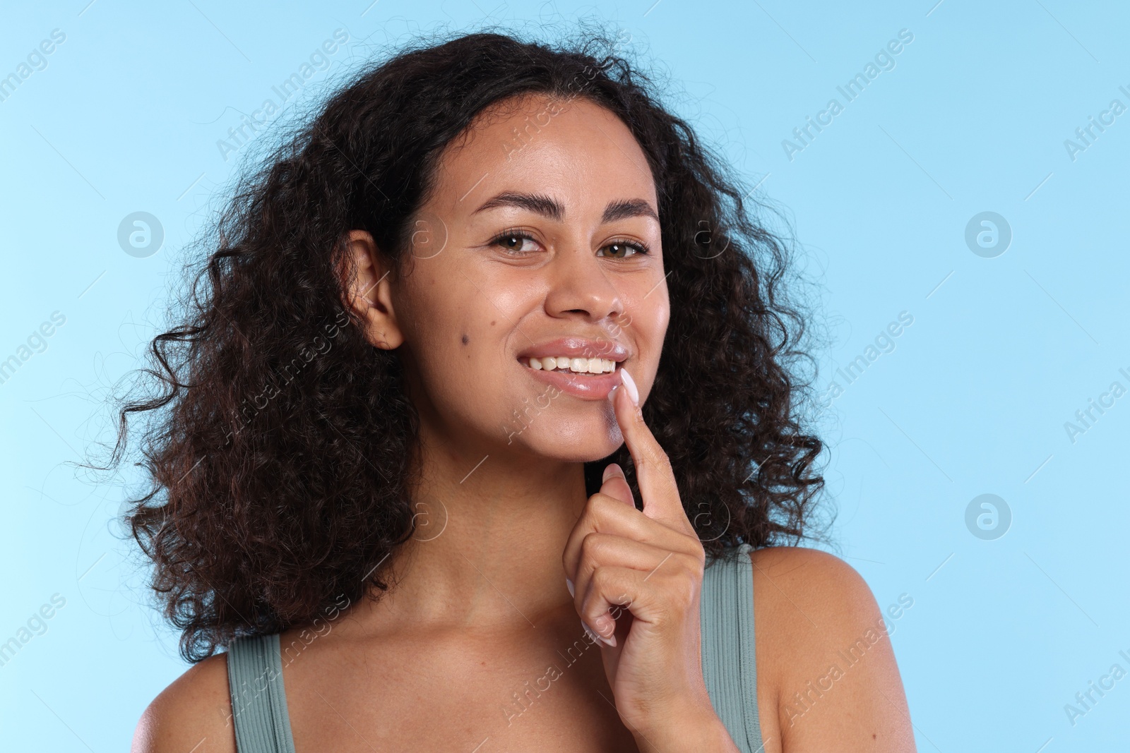 Smiling woman applying lip balm onto her lips on light blue background Photo of Smiling woman applying lip balm onto her lips on light blue background
