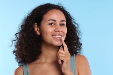 Photo of Smiling woman applying lip balm onto her lips on light blue background
