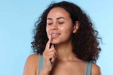 Photo of Smiling woman applying lip balm onto her lips on light blue background