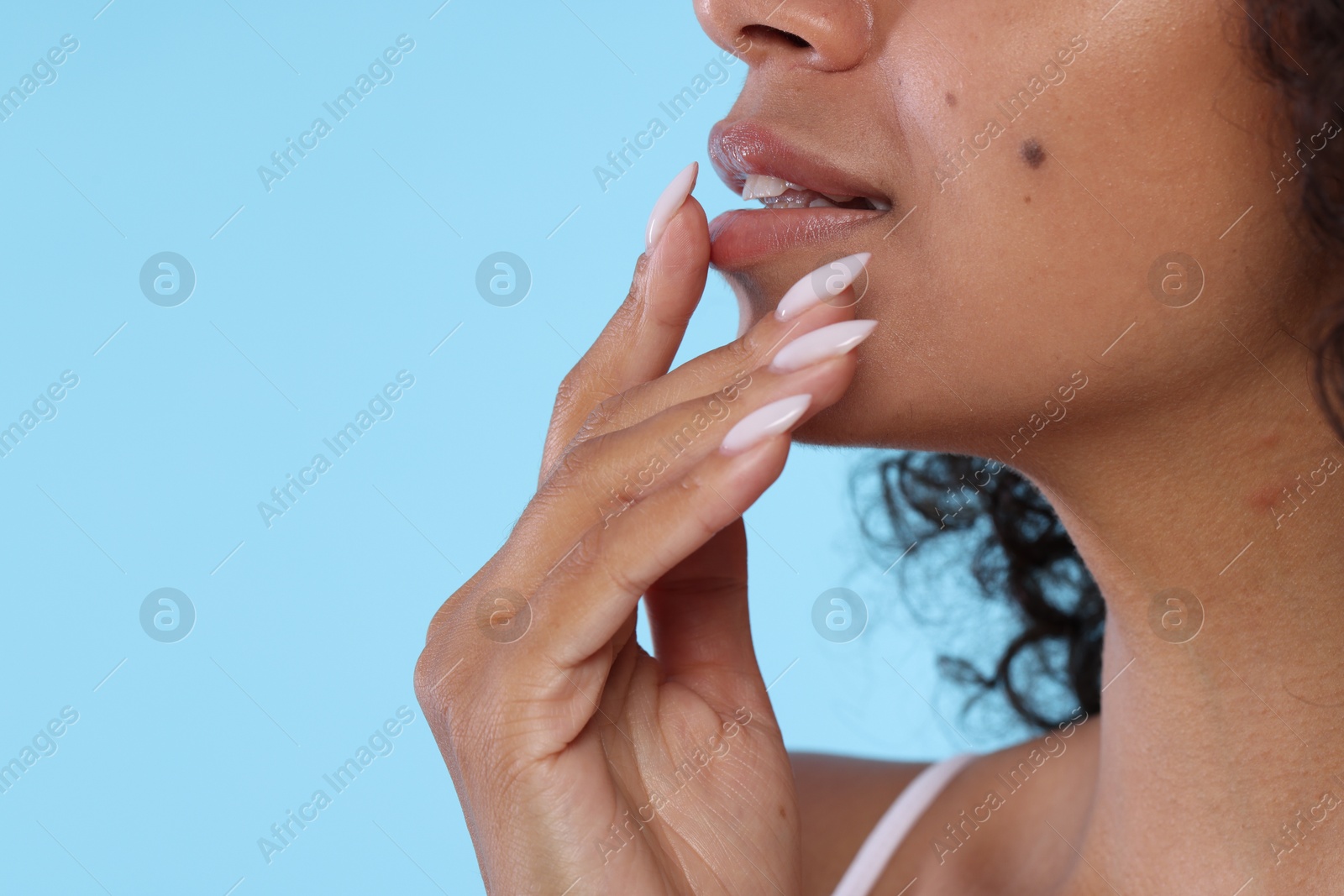Smiling woman applying lip balm onto her lips on light blue background, closeup. Space for text Photo of Smiling woman applying lip balm onto her lips on light blue background, closeup. Space for text