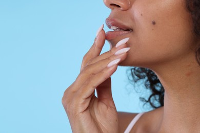 Photo of Smiling woman applying lip balm onto her lips on light blue background, closeup. Space for text