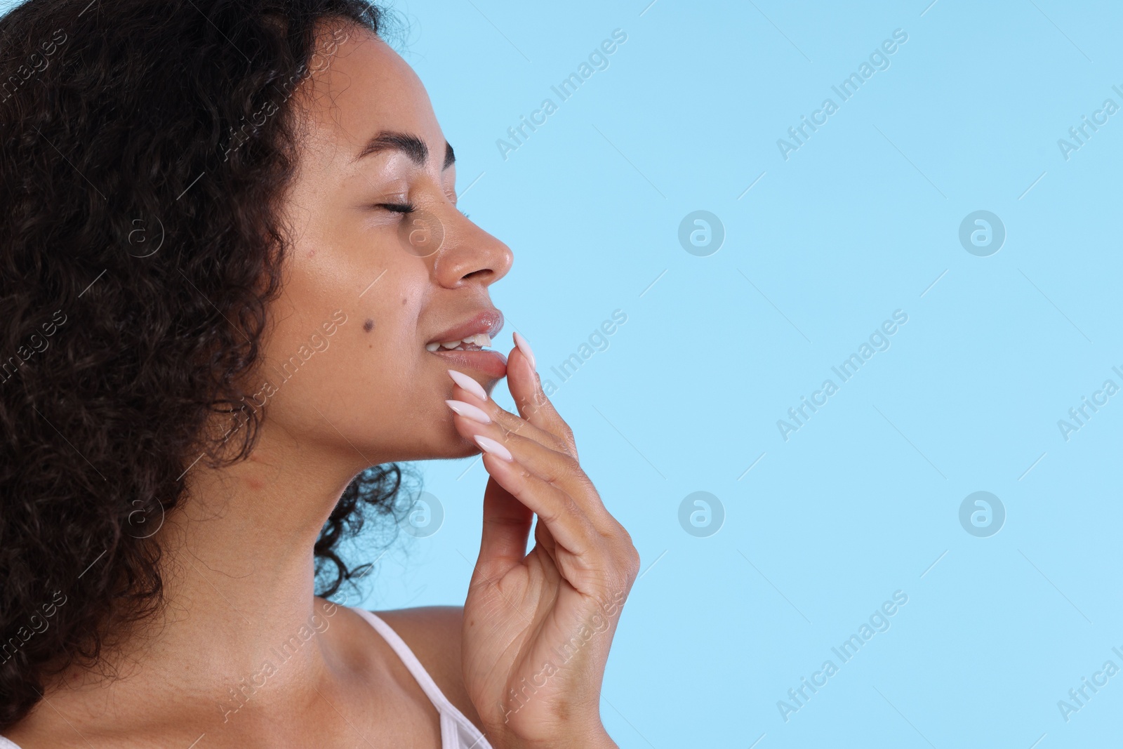 Smiling woman applying lip balm onto her lips on light blue background, closeup. Space for text Photo of Smiling woman applying lip balm onto her lips on light blue background, closeup. Space for text