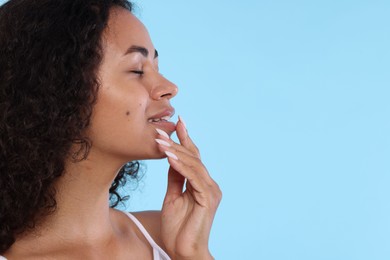 Photo of Smiling woman applying lip balm onto her lips on light blue background, closeup. Space for text