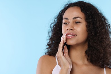 Photo of Smiling woman applying lip balm onto her lips on light blue background. Space for text