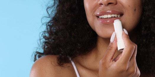 Photo of Smiling woman applying lip balm onto her lips on light blue background, closeup