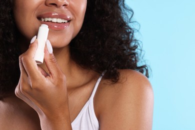 Photo of Smiling woman applying lip balm onto her lips on light blue background, closeup
