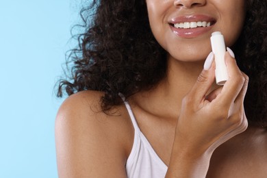 Photo of Smiling woman applying lip balm onto her lips on light blue background, closeup