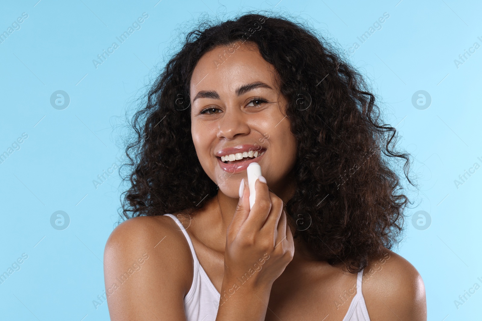 Smiling woman applying lip balm onto her lips on light blue background Photo of Smiling woman applying lip balm onto her lips on light blue background