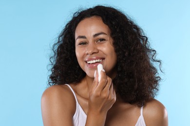 Photo of Smiling woman applying lip balm onto her lips on light blue background
