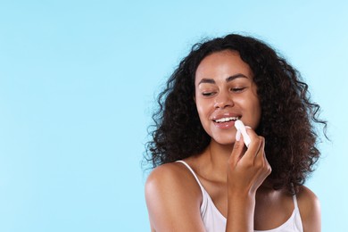 Photo of Smiling woman applying lip balm onto her lips on light blue background. Space for text