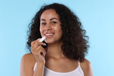 Photo of Smiling woman applying lip balm onto her lips on light blue background