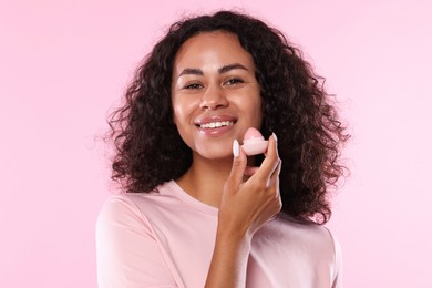 Photo of Smiling woman with lip balm on pink background