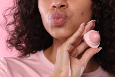 Photo of Woman with container of lip balm on pink background, closeup