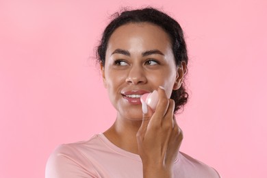 Photo of Smiling woman applying lip balm onto her lips on pink background