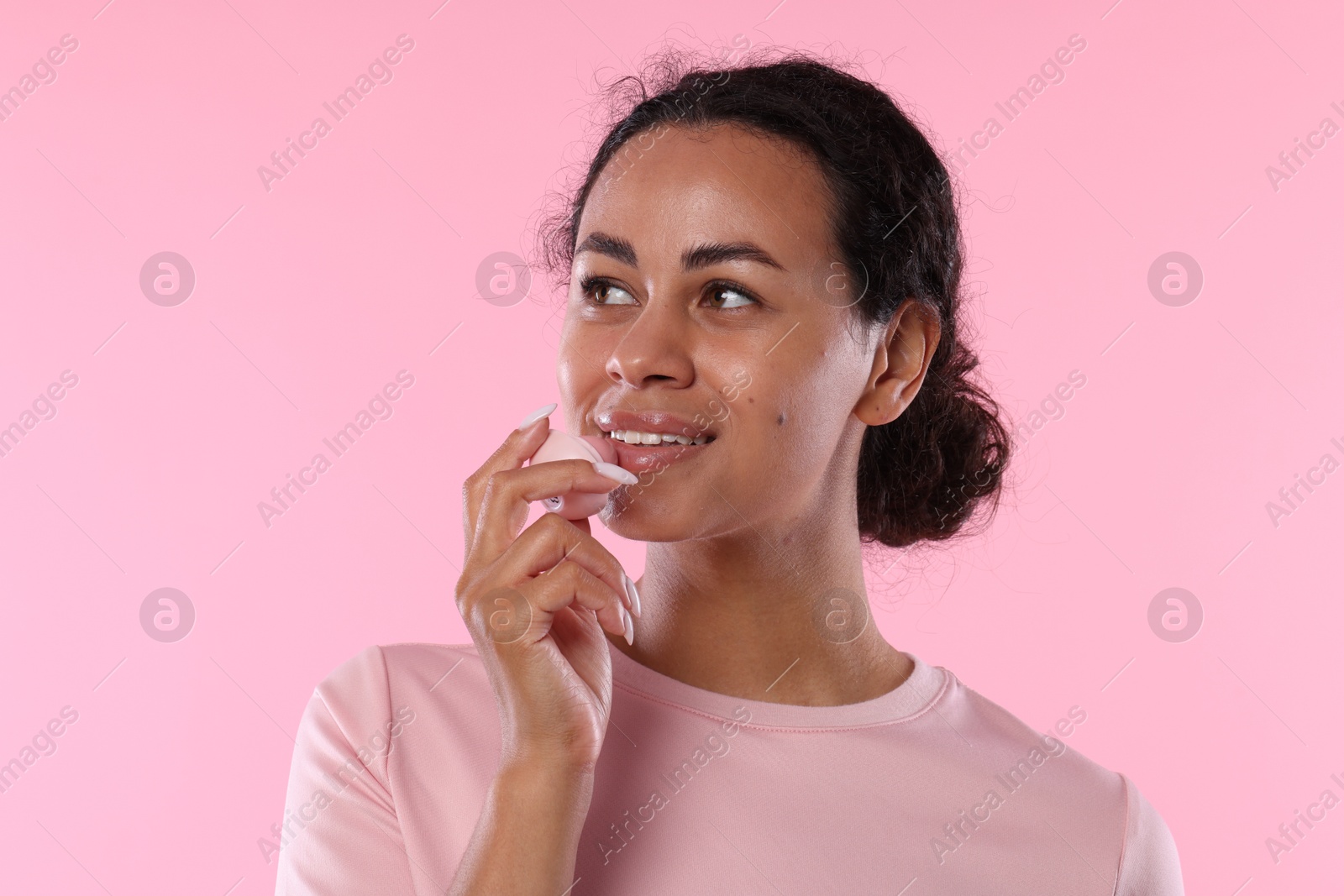 Smiling woman applying lip balm onto her lips on pink background Photo of Smiling woman applying lip balm onto her lips on pink background