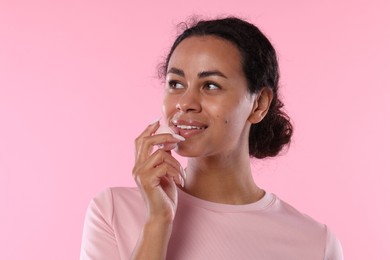 Photo of Smiling woman applying lip balm onto her lips on pink background