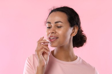 Photo of Smiling woman applying lip balm onto her lips on pink background