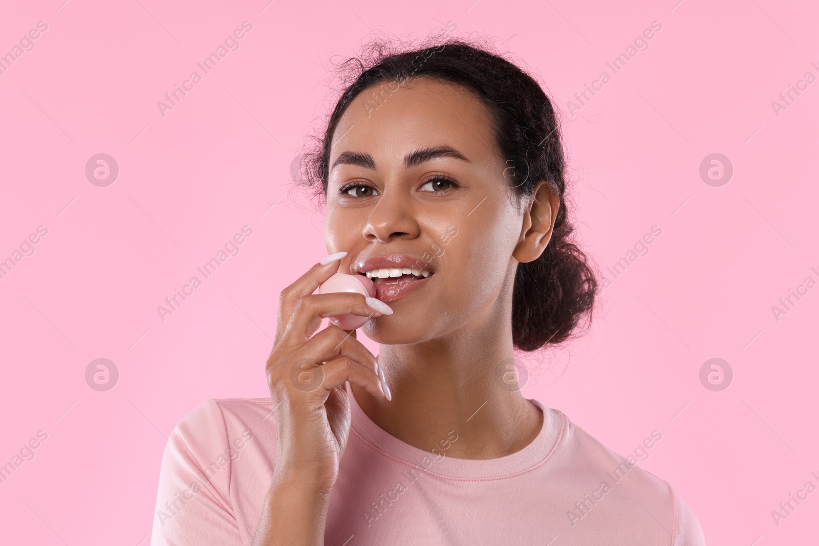 Smiling woman applying lip balm onto her lips on pink background Photo of Smiling woman applying lip balm onto her lips on pink background