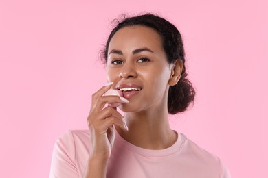Photo of Smiling woman applying lip balm onto her lips on pink background