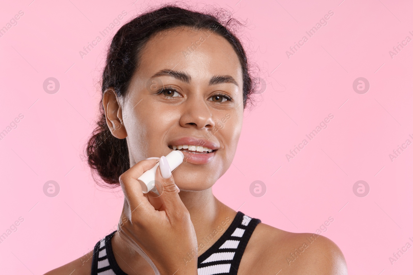 Smiling woman applying lip balm onto her lips on pink background, closeup Photo of Smiling woman applying lip balm onto her lips on pink background, closeup