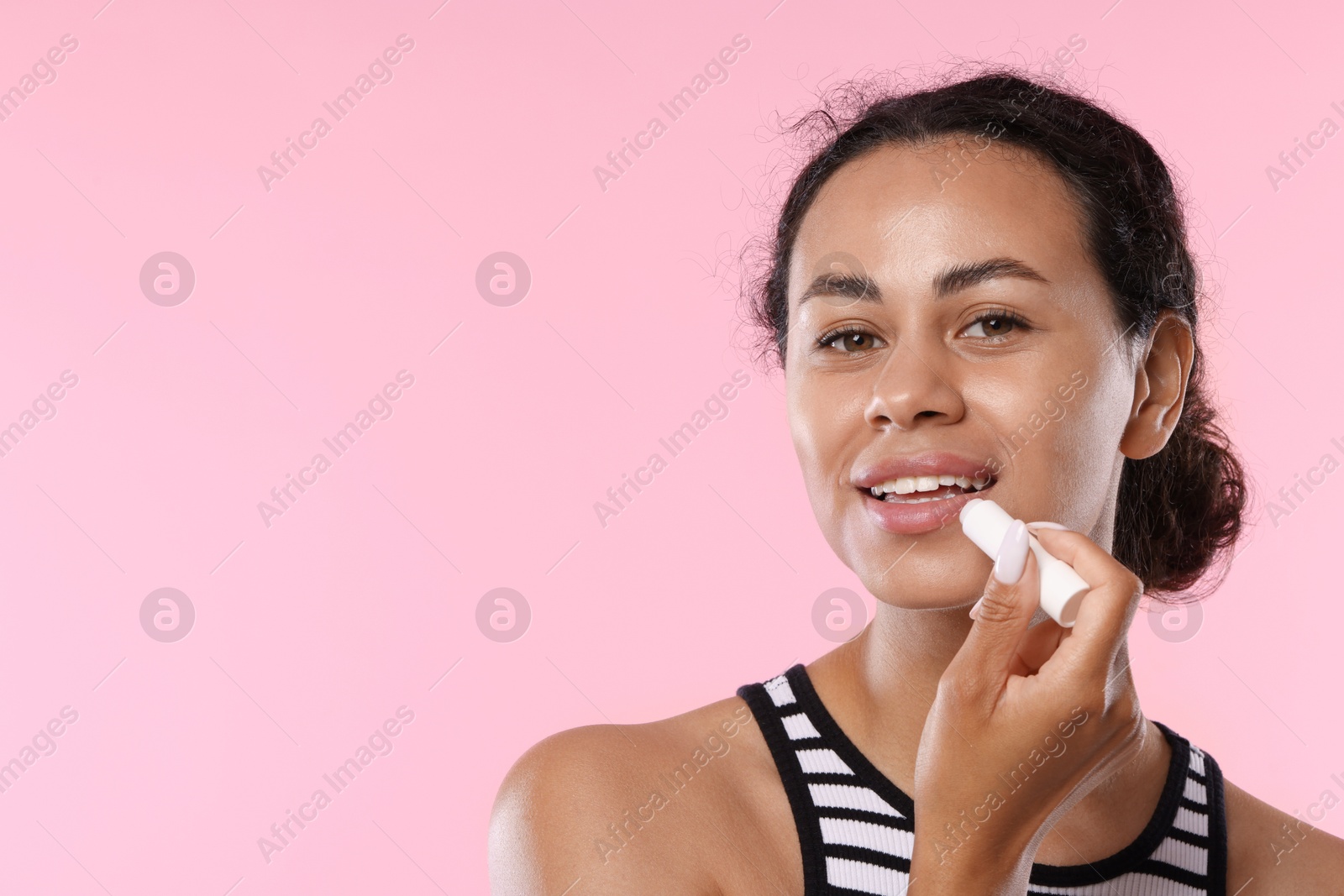 Smiling woman applying lip balm onto her lips on pink background. Space for text Photo of Smiling woman applying lip balm onto her lips on pink background. Space for text