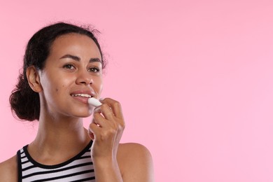 Photo of Smiling woman applying lip balm onto her lips on pink background. Space for text