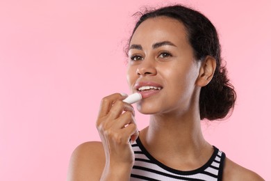 Photo of Smiling woman applying lip balm onto her lips on pink background