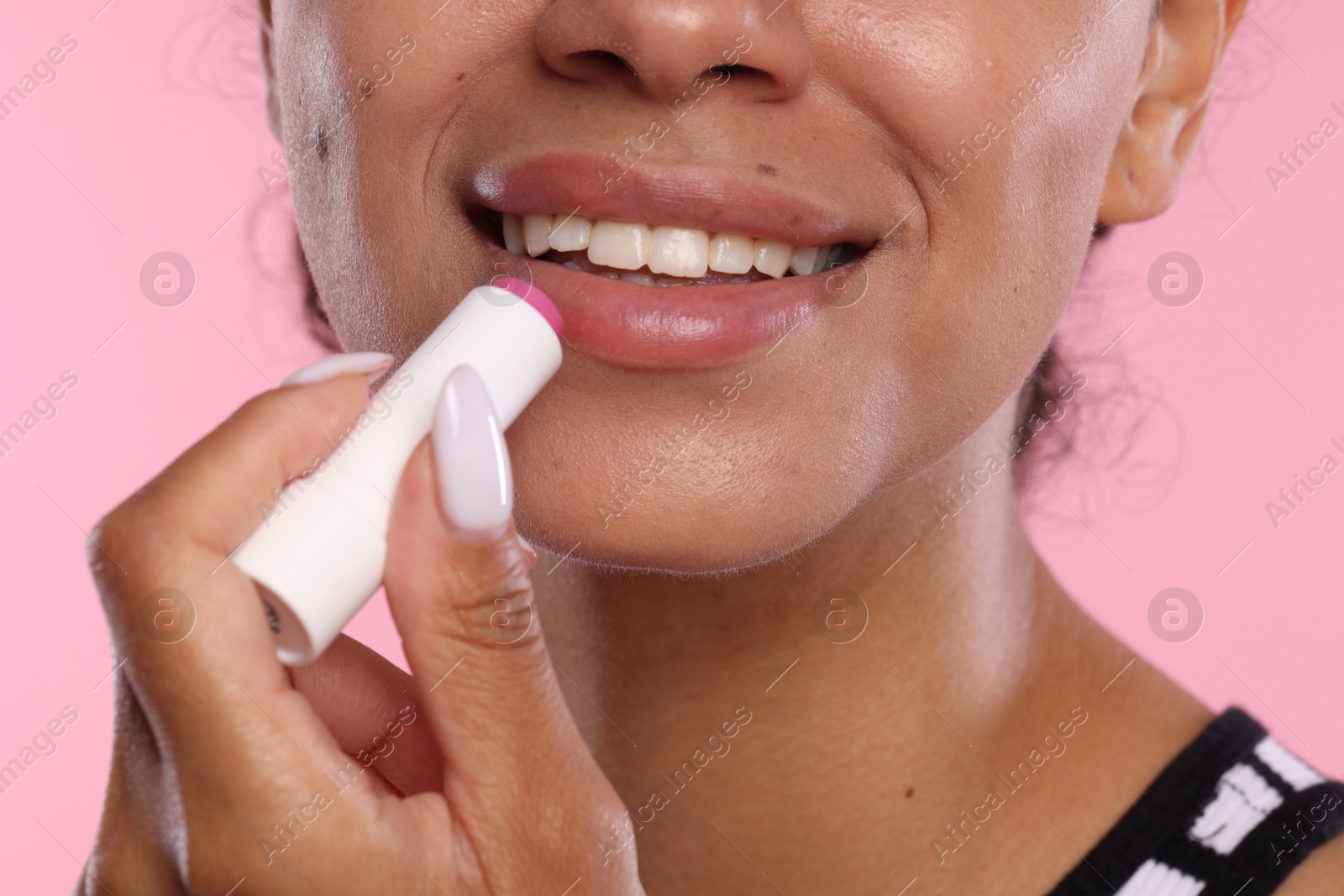 Smiling woman applying lip balm onto her lips on pink background, closeup Photo of Smiling woman applying lip balm onto her lips on pink background, closeup