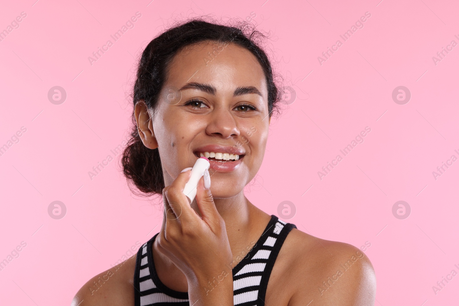 Smiling woman applying lip balm onto her lips on pink background Photo of Smiling woman applying lip balm onto her lips on pink background