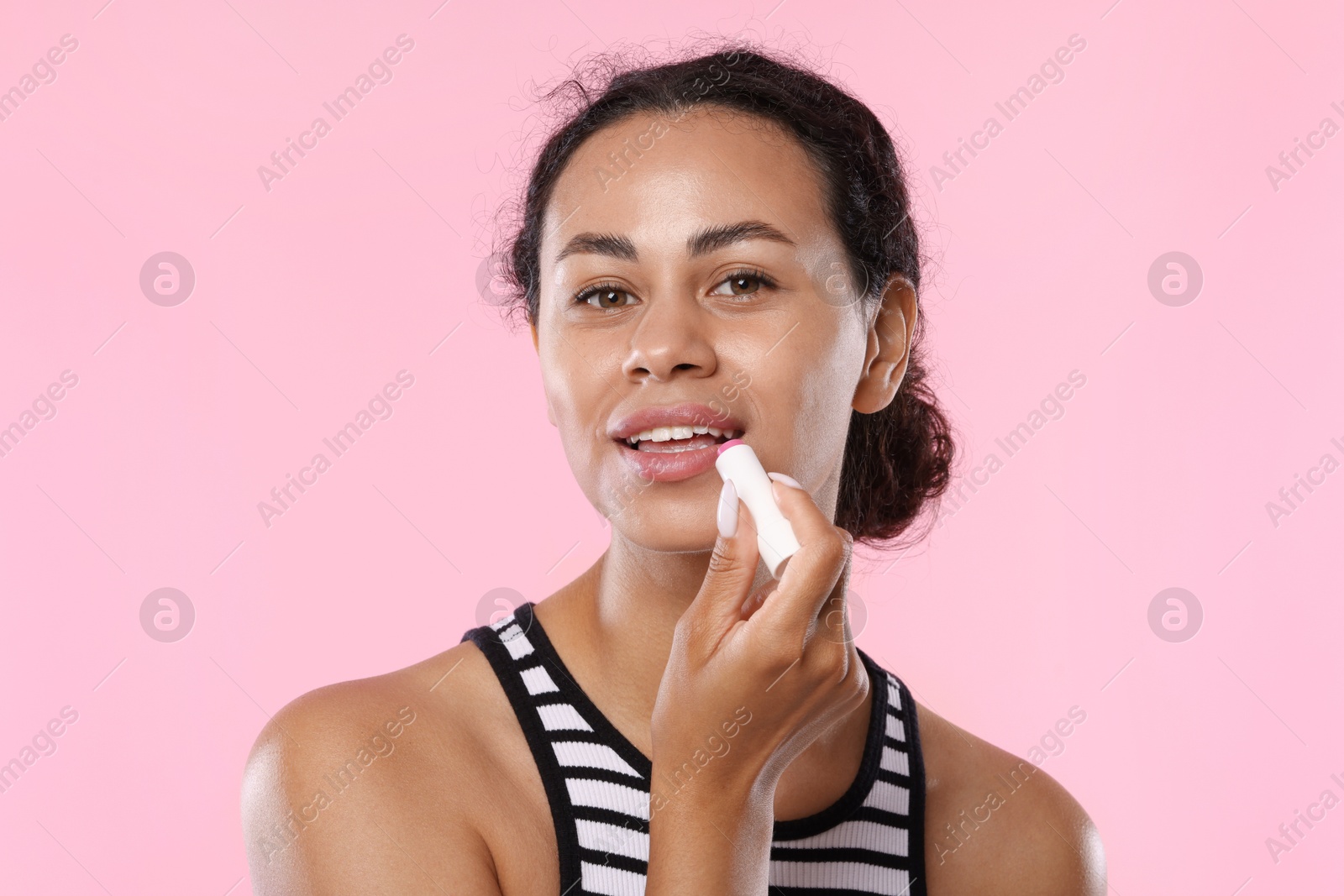 Smiling woman applying lip balm onto her lips on pink background Photo of Smiling woman applying lip balm onto her lips on pink background