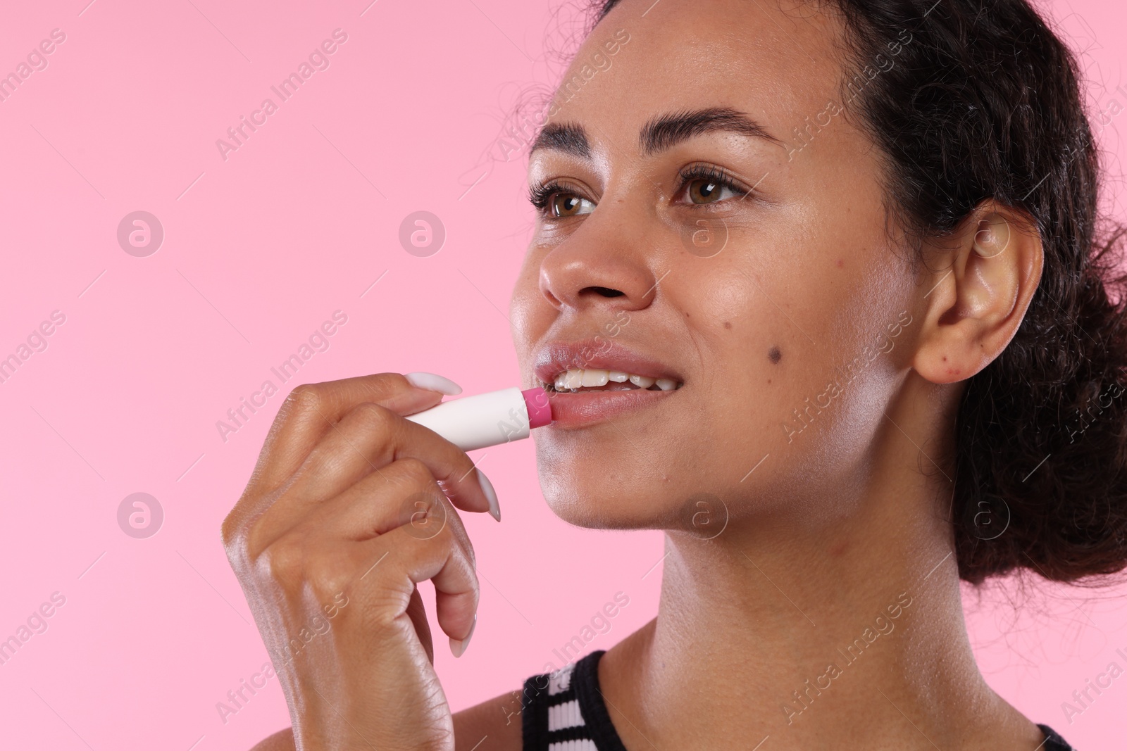 Smiling woman applying lip balm onto her lips on pink background, closeup Photo of Smiling woman applying lip balm onto her lips on pink background, closeup