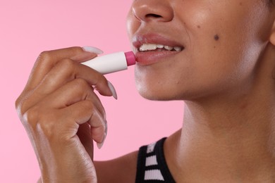 Photo of Smiling woman applying lip balm onto her lips on pink background, closeup