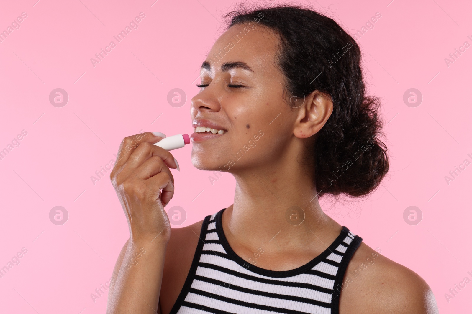 Smiling woman applying lip balm onto her lips on pink background Photo of Smiling woman applying lip balm onto her lips on pink background